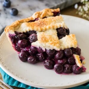 Slice of blueberry pie with a lattice crust on a white plate.