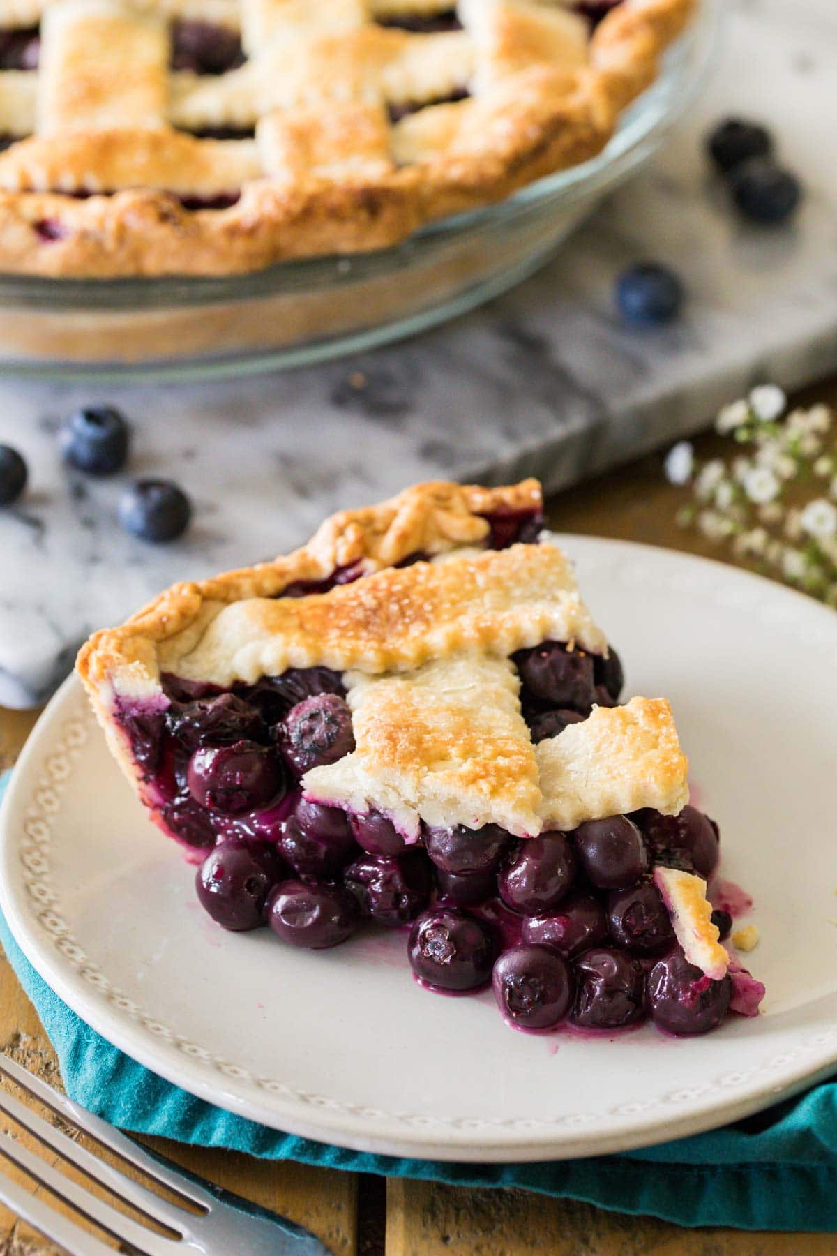 Slice of blueberry pie with a lattice crust on a white plate.