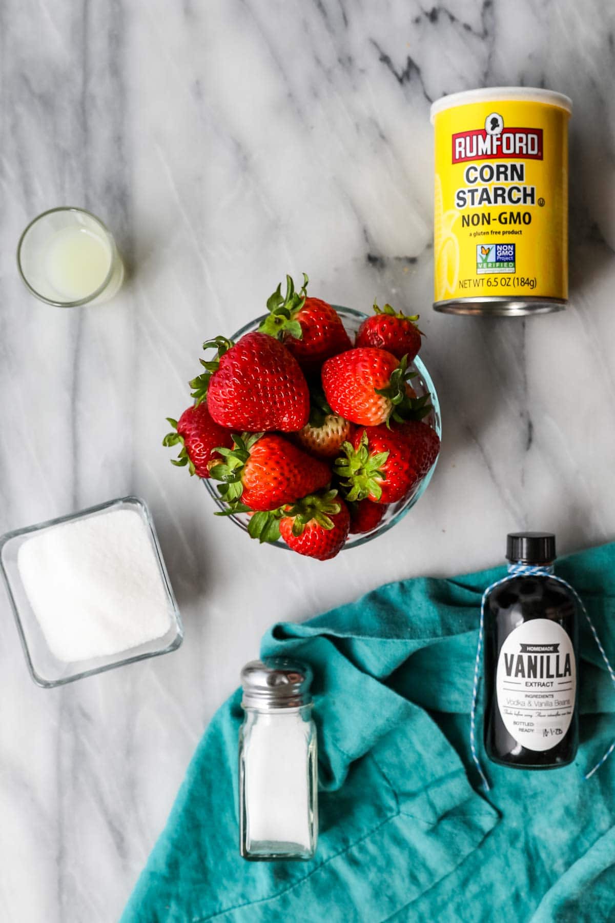 Overhead view of ingredients including strawberries, cornstarch, lemon juice, sugar, salt, and vanilla.