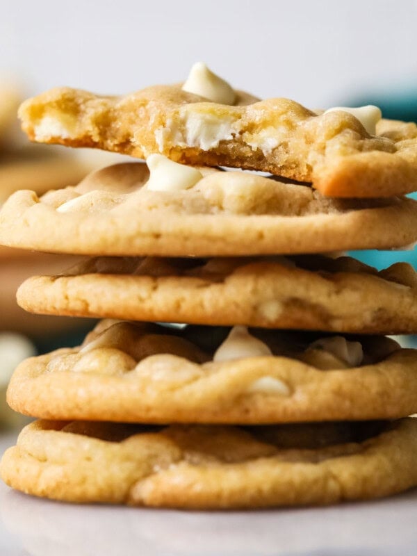 Stack of white chocolate chip cookies with the top cookie missing a bite.