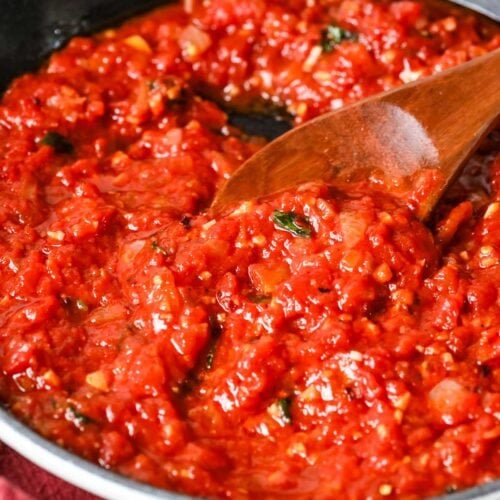 Pot of arrabiata sauce being stirred with a wood spoon.
