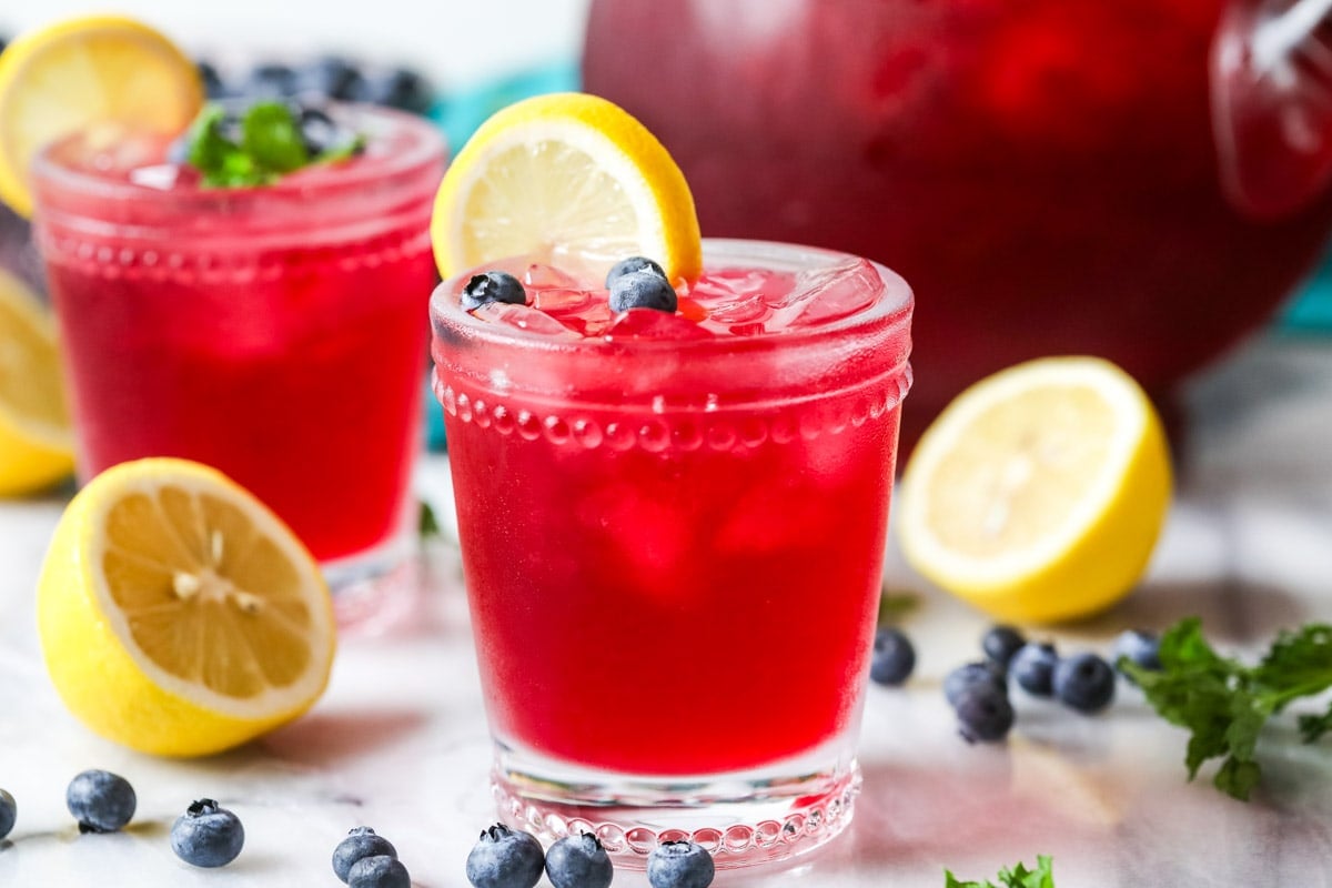 Glasses of lemonade made with blueberry syrup garnished with lemon slices, blueberries, and mint.