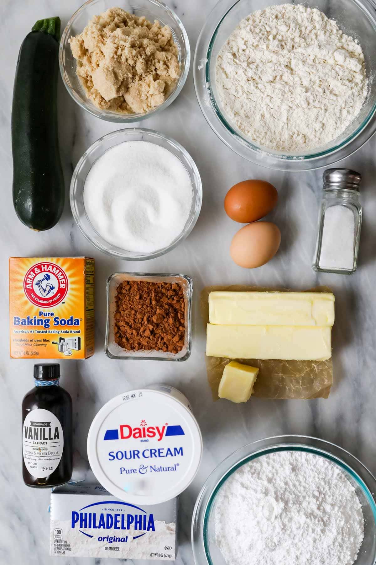 Overhead view of ingredients including zucchini, brown sugar, sour cream, cocoa powder, and more.