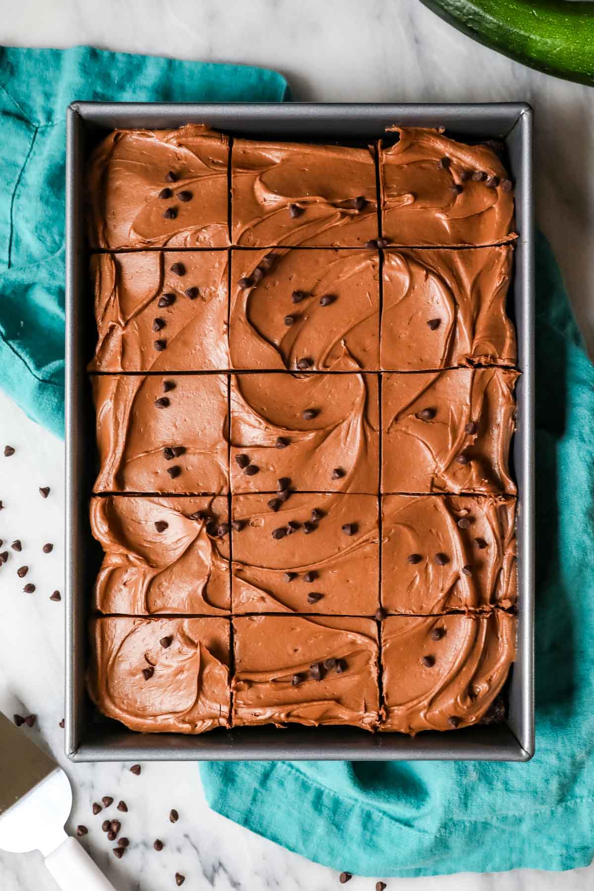 Overhead view of a frosted chocolate cake that's been cut into squares in a pan.