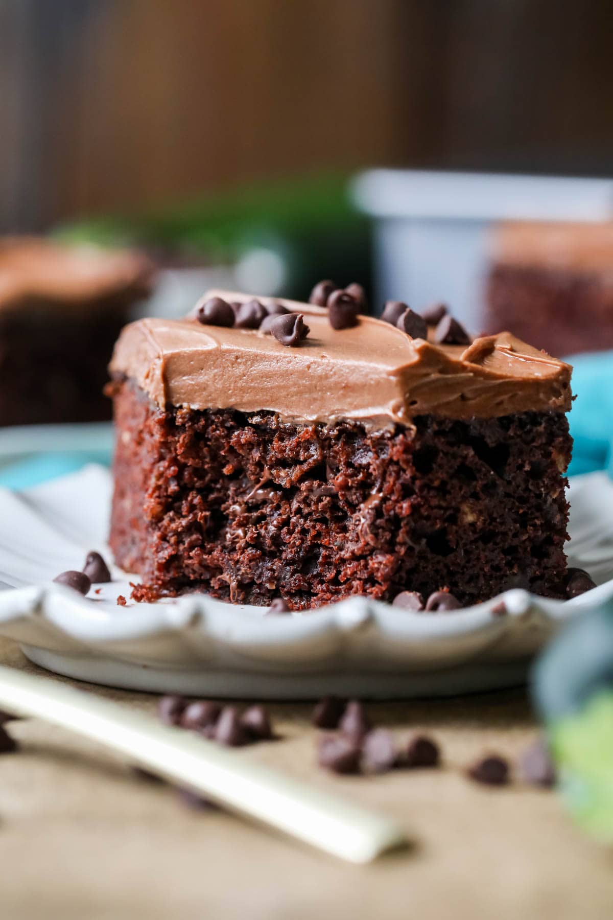 Slice of frosted chocolate zucchini cake on a white plate.