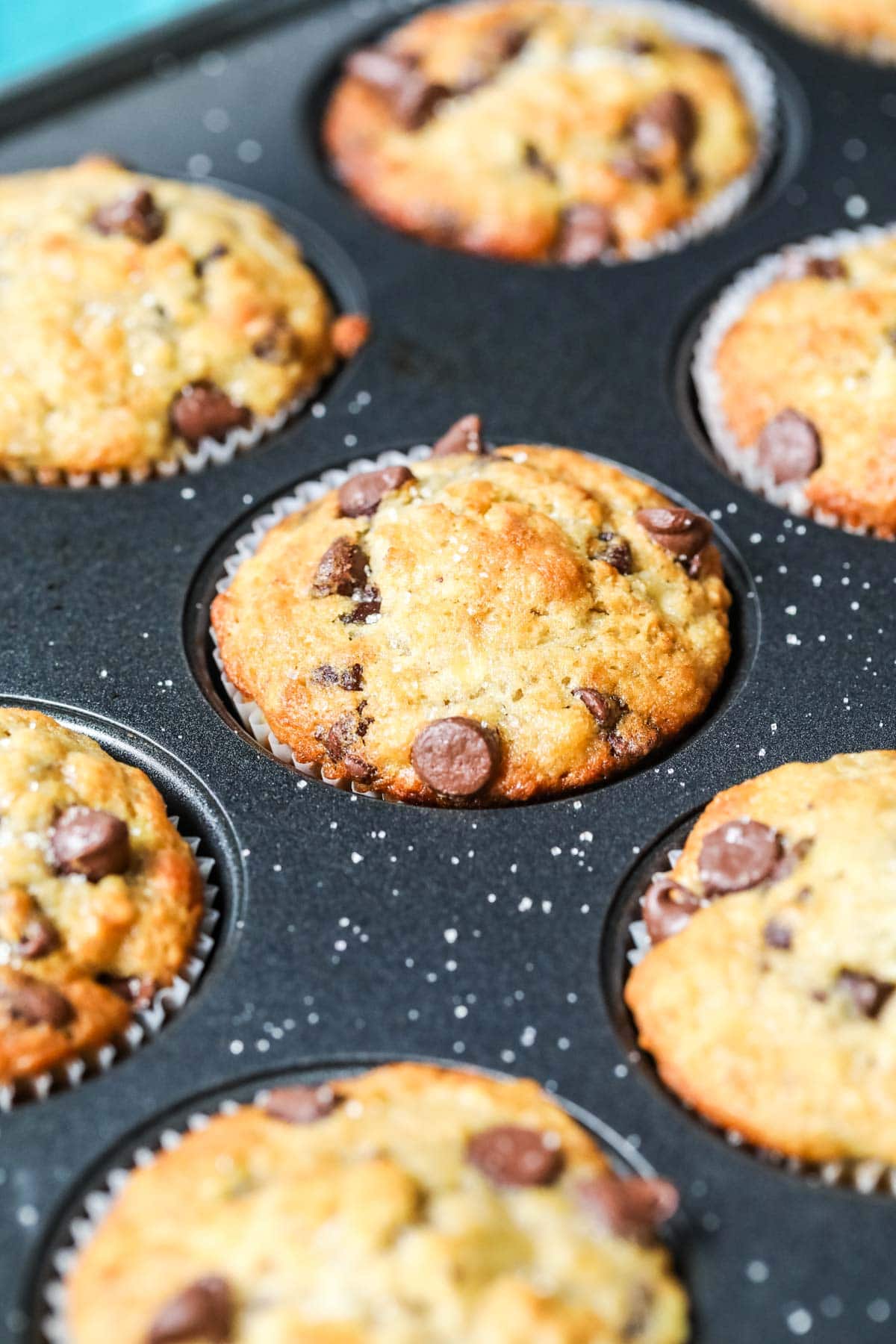 Muffin tray with golden brown, sugar dusted banana chocolate chip muffins inside.