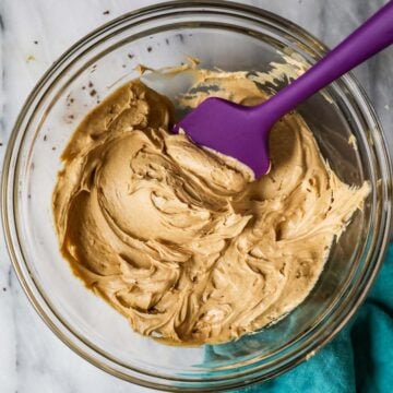 Overhead view of a bowl of coffee frosting with a purple spatula.