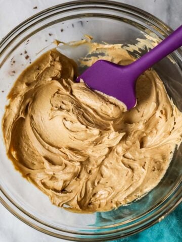 Overhead view of a bowl of coffee frosting with a purple spatula.