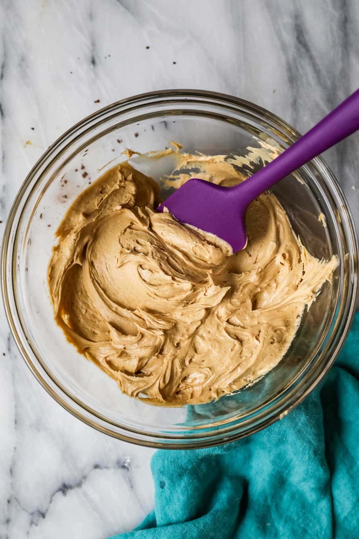 Overhead view of a bowl of coffee frosting with a purple spatula.