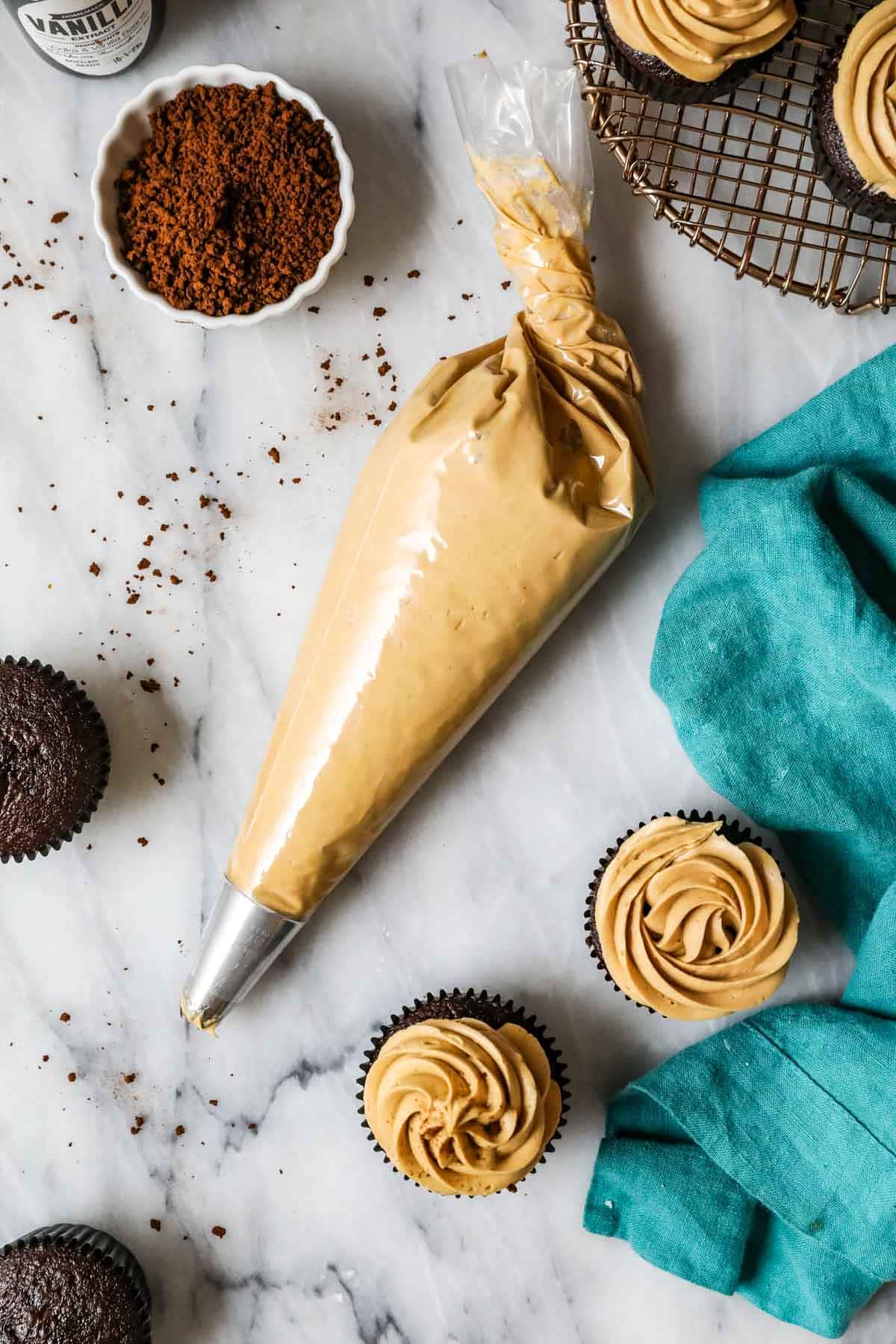 Overhead view of a piping bag of coffee frosting beside two frosted cupcakes.