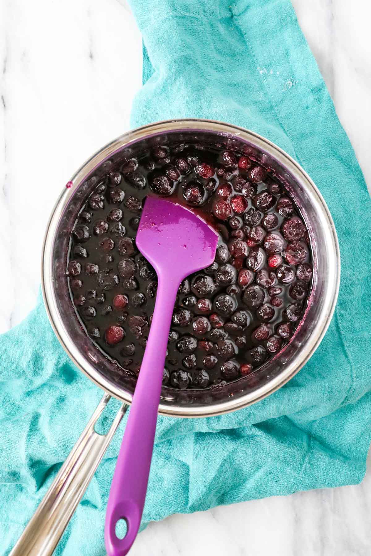 Overhead view of blueberries cooking in a saucepan with sugar and water.