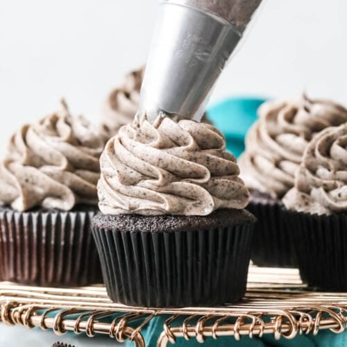 Oreo frosting being piped onto a dark chocolate cupcake that's surrounded by other frosted cupcakes.