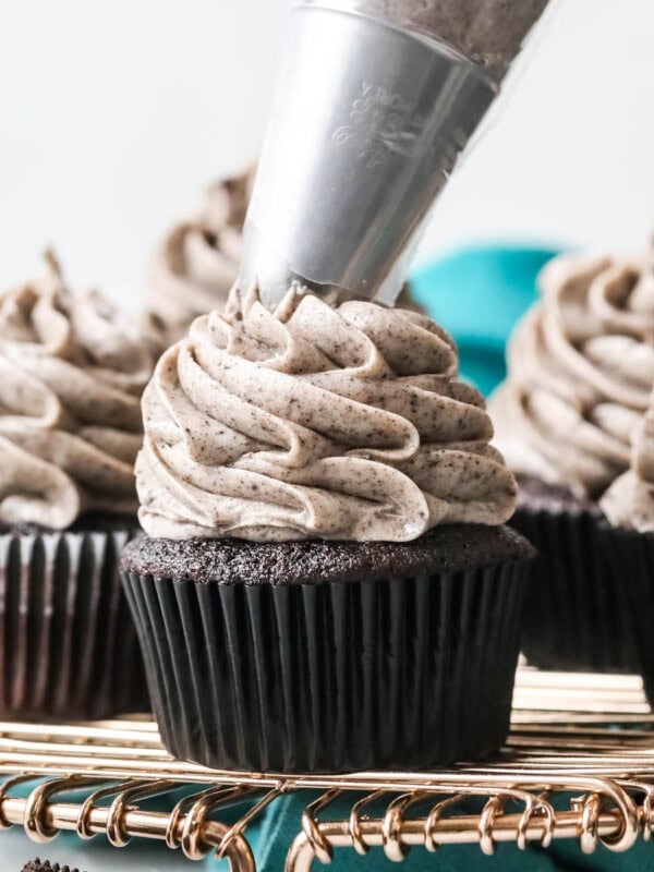Oreo frosting being piped onto a dark chocolate cupcake that's surrounded by other frosted cupcakes.