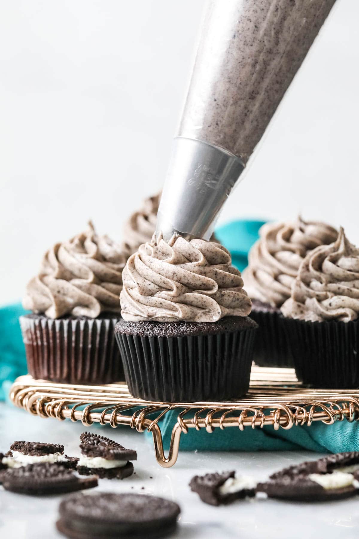 Oreo frosting being piped onto a dark chocolate cupcake that's surrounded by other frosted cupcakes.