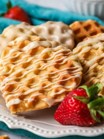 Heart shaped waffle cookies with a drizzled maple glaze on a white plate with a strawberry.
