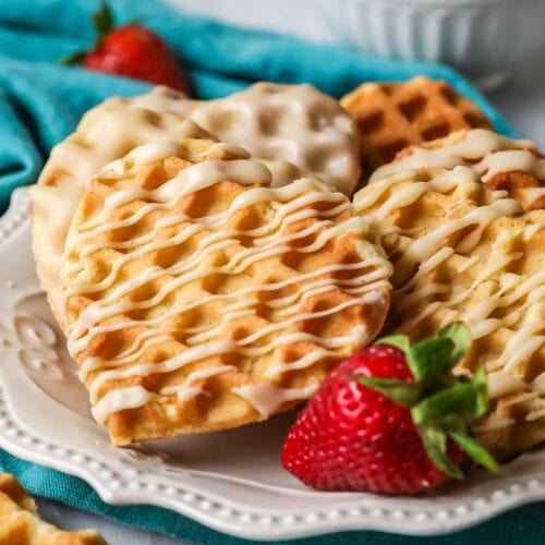 Heart shaped waffle cookies with a drizzled maple glaze on a white plate with a strawberry.