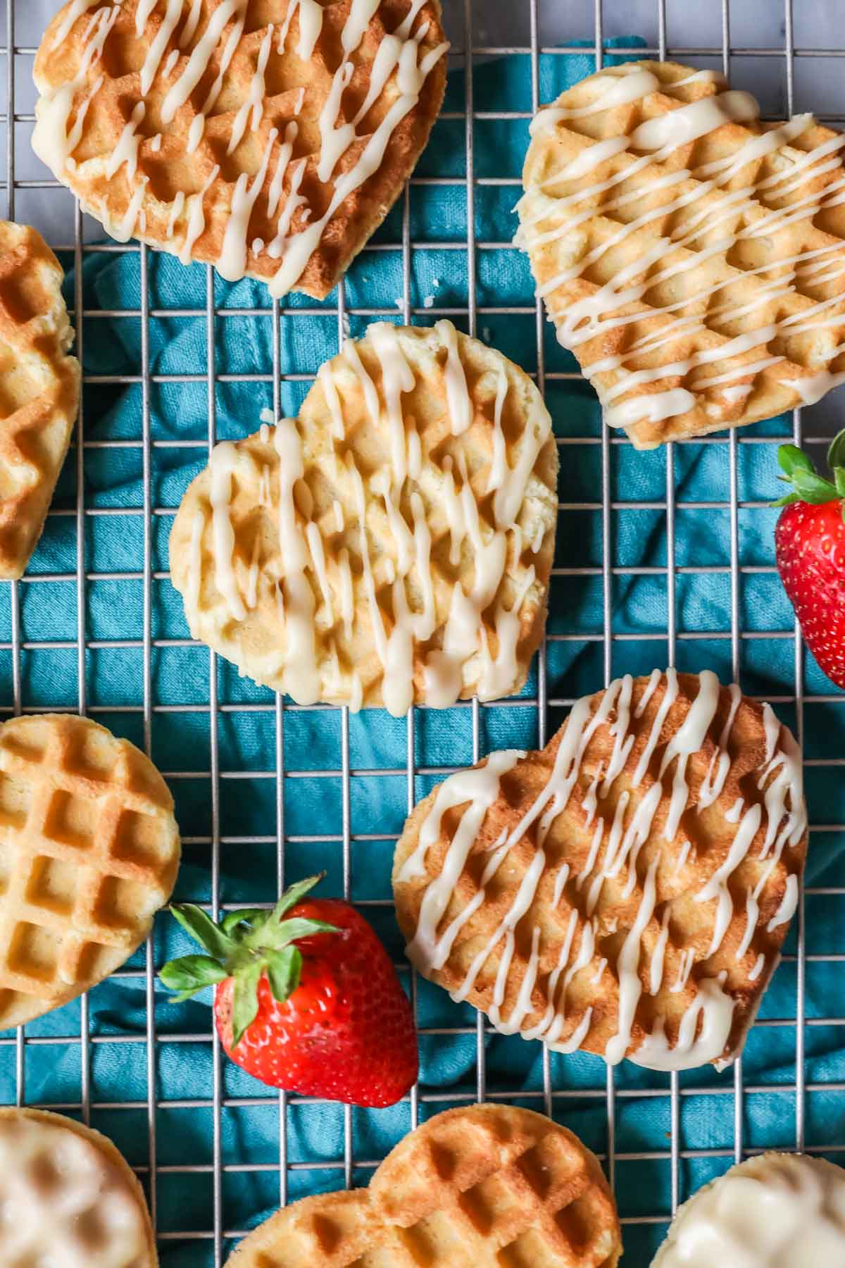Overhead view of heart shaped waffle cookies on a cooling rack with a turquoise tea towel underneath.