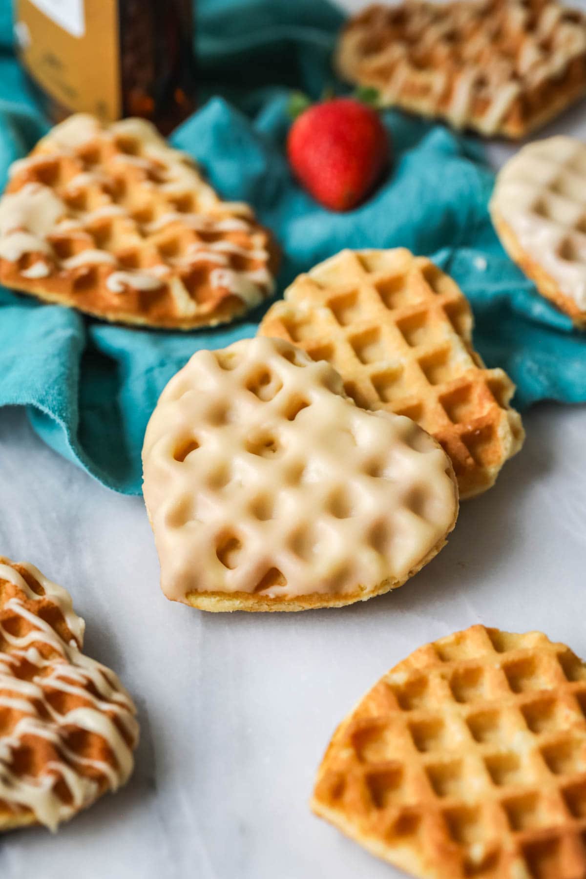 Waffle cookie that's been dipped in glaze surrounded by other cookies that are drizzled with glaze.