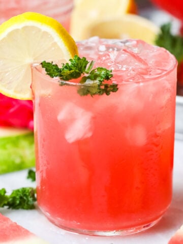 Glass of watermelon lemonade garnished with fresh mint and lemon slices.
