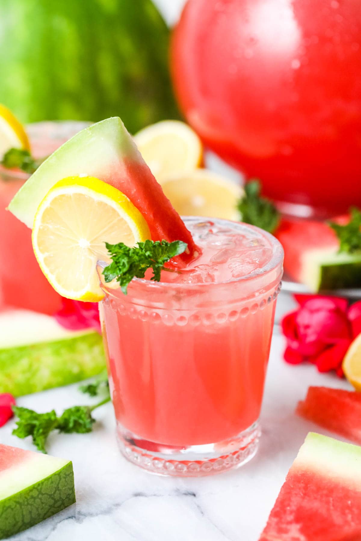Glass of watermelon lemonade garnished with mint leaves, watermelon slices, and lemon slices.