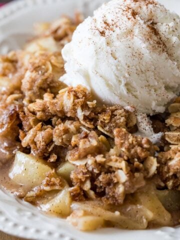 Bowl of apple crisp topped with a scoop of vanilla ice cream and cinnamon.