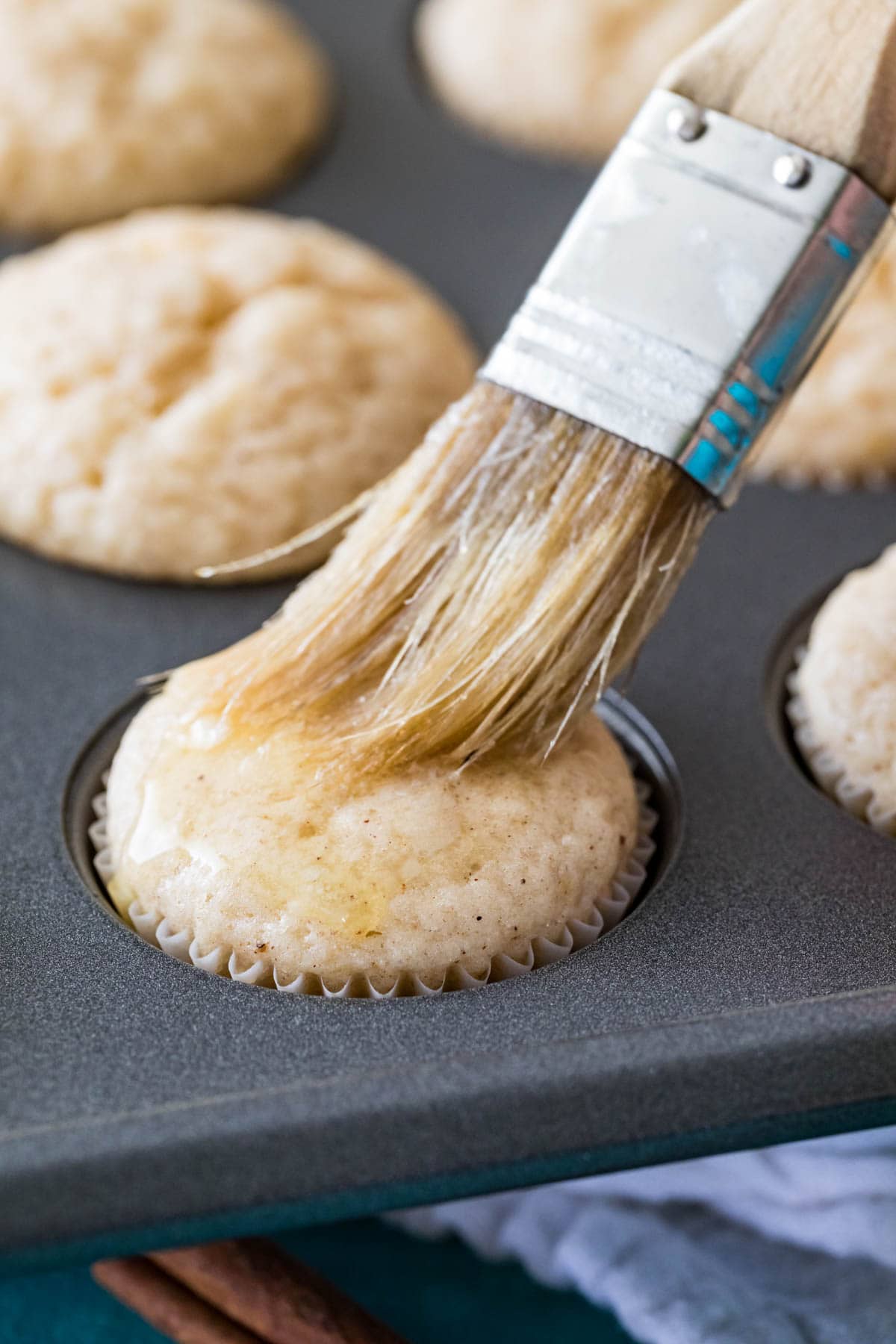 Pastry brush brushing melted butter over mini muffins.