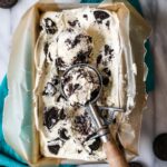 Overhead view of a pan of cookies and cream ice cream with an ice cream scooper resting on top.