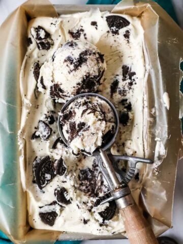 Overhead view of a pan of cookies and cream ice cream with an ice cream scooper resting on top.
