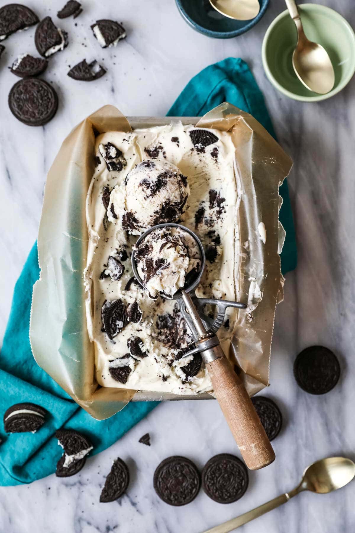 Overhead view of a pan of cookies and cream ice cream with an ice cream scooper resting on top.