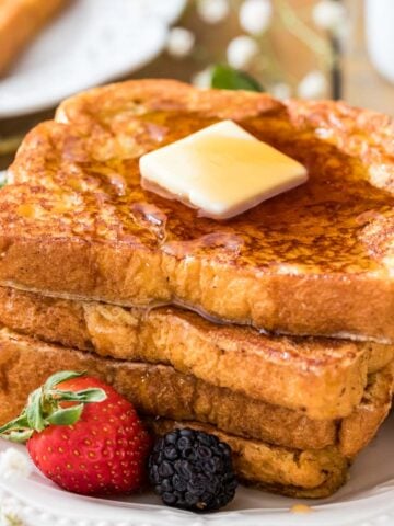 Stack of french toast with butter on top and berries scattered around.