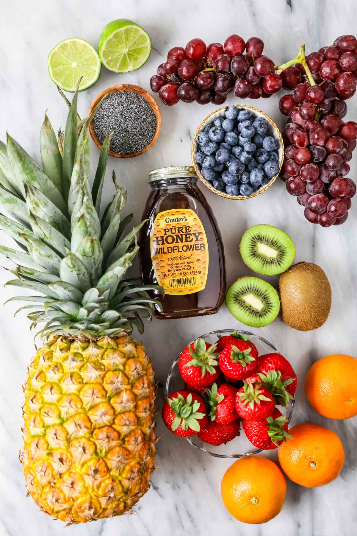 Overhead view of ingredients including pineapple, grapes, kiwi, honey, and more.