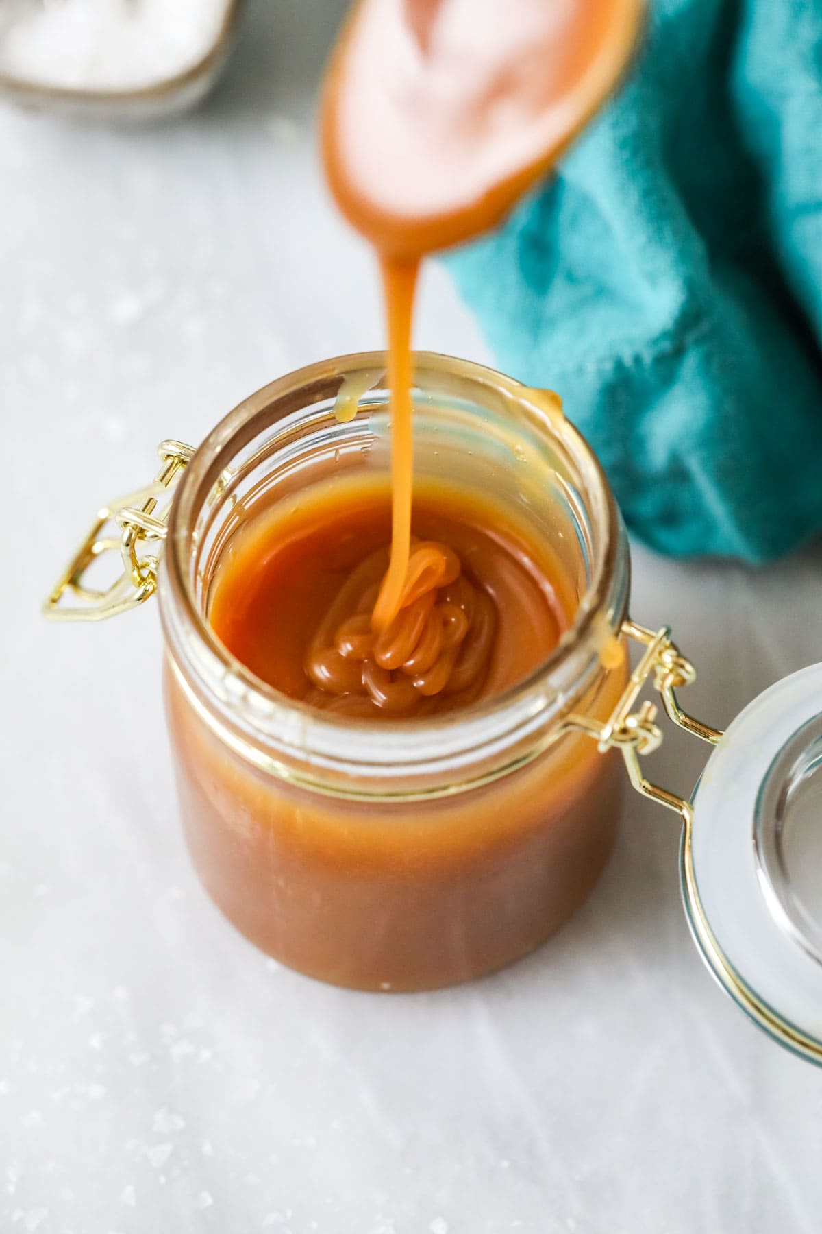 Overhead view of caramel dripping off a spoon into a jar.