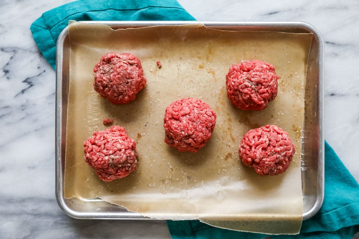 Overhead view of round burger patties on a parchment lined baking sheet.