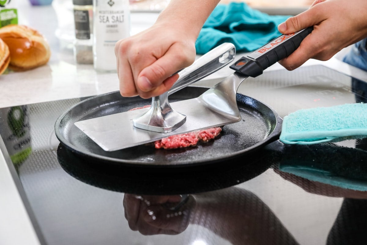 Photo of a burger in a pan being smashed beneath a press.