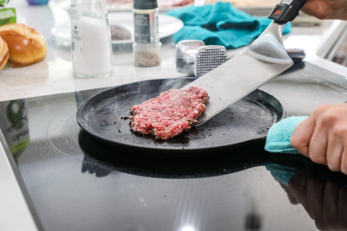 Large spatula flipping a thin burger on a griddle.