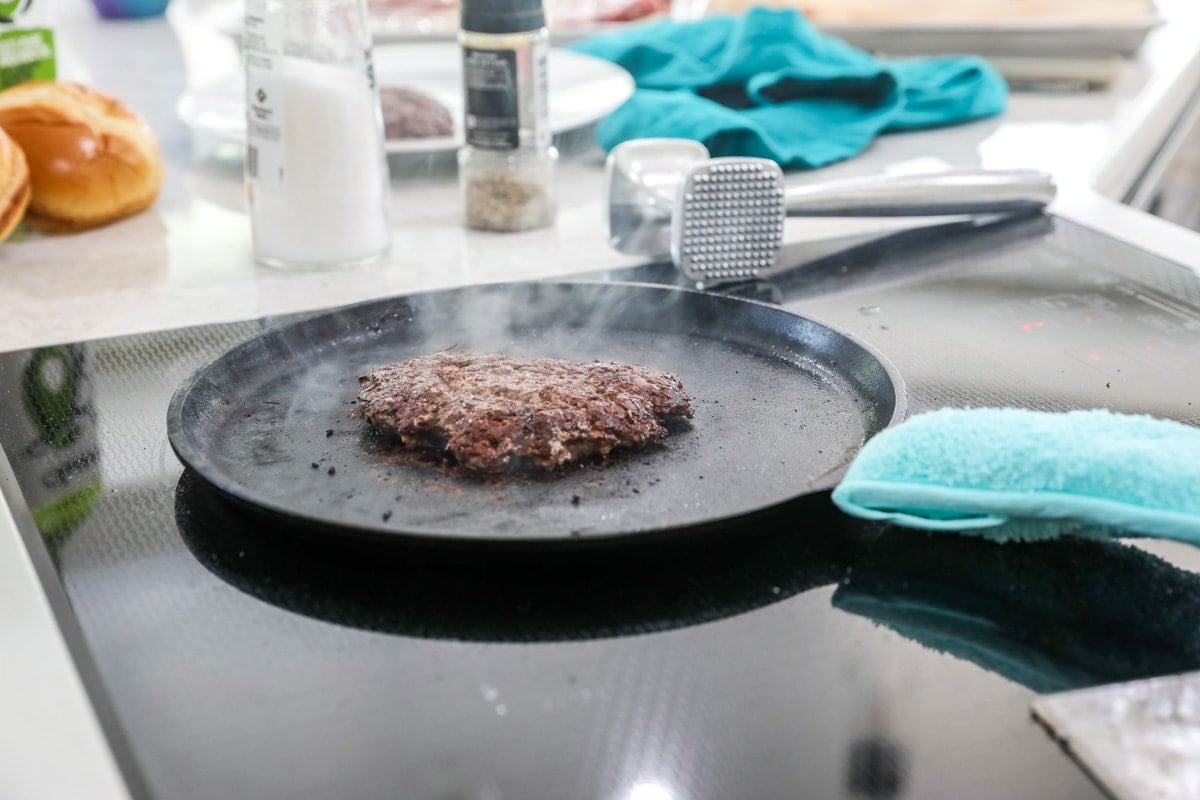 Thin burger cooking on a hot griddle.