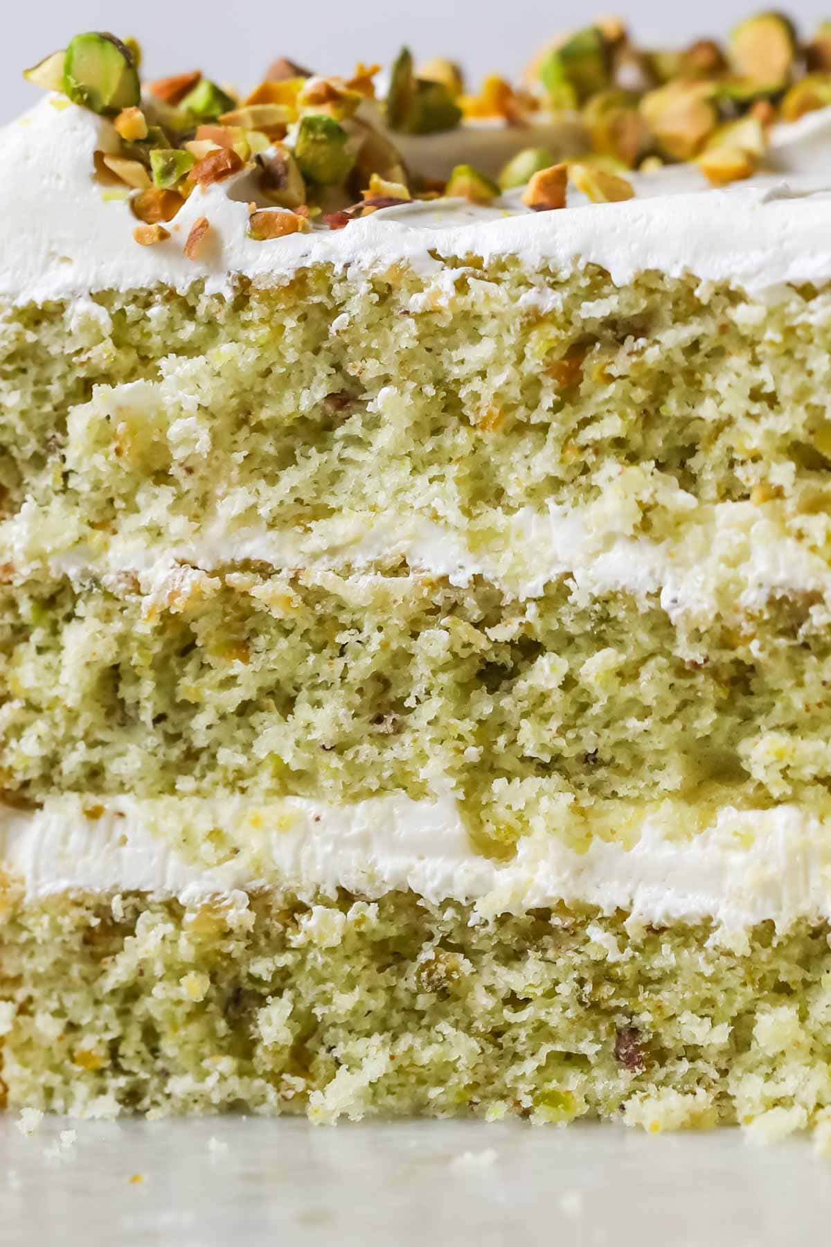 Close-up view of a slice of pistachio cake made with three layers of green cake and a swiss meringue buttercream frosting.