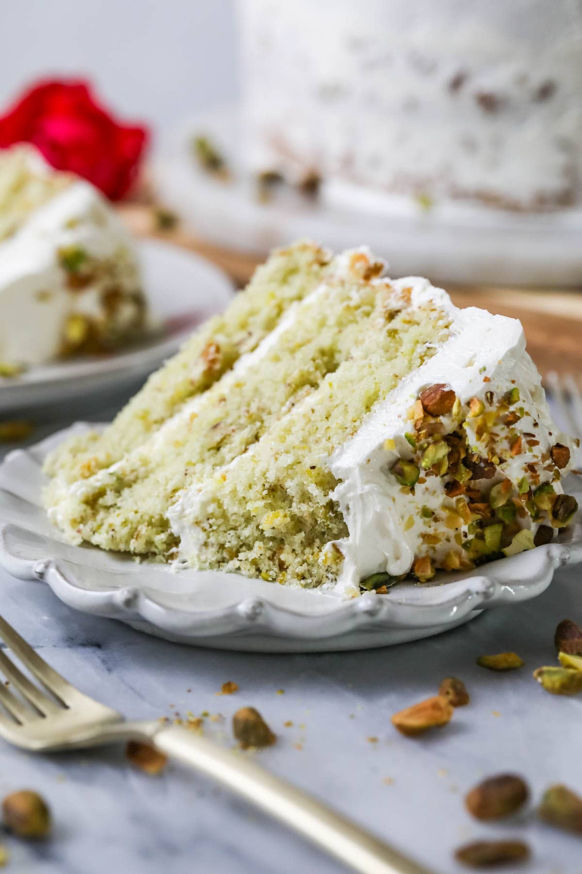 Slice of pale green layer cake made with pistachios on a white plate with one bite missing.