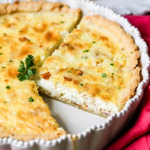 Quiche lorraine in a pan with several slices cut into it.