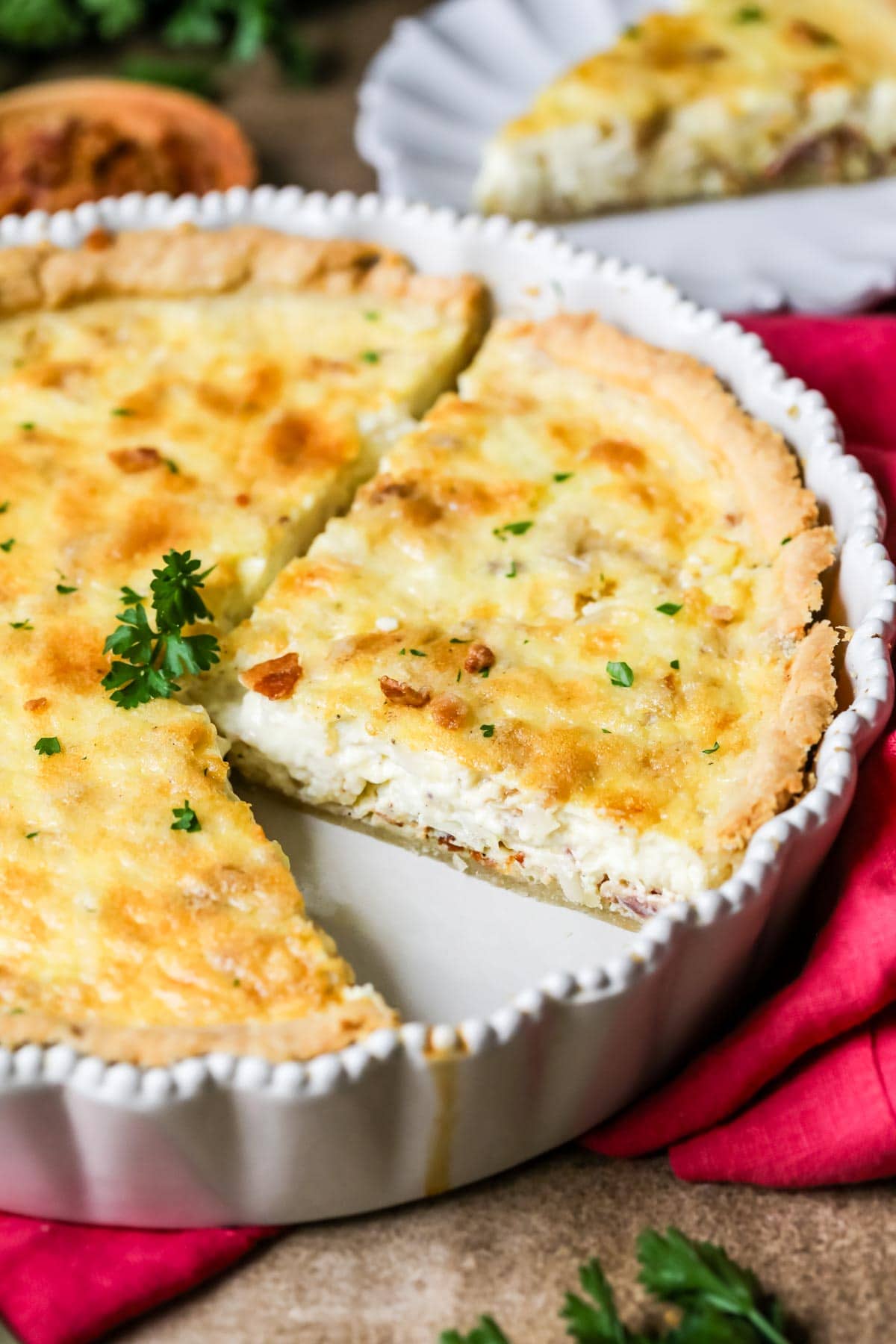 Quiche lorraine in a pan with several slices cut into it.