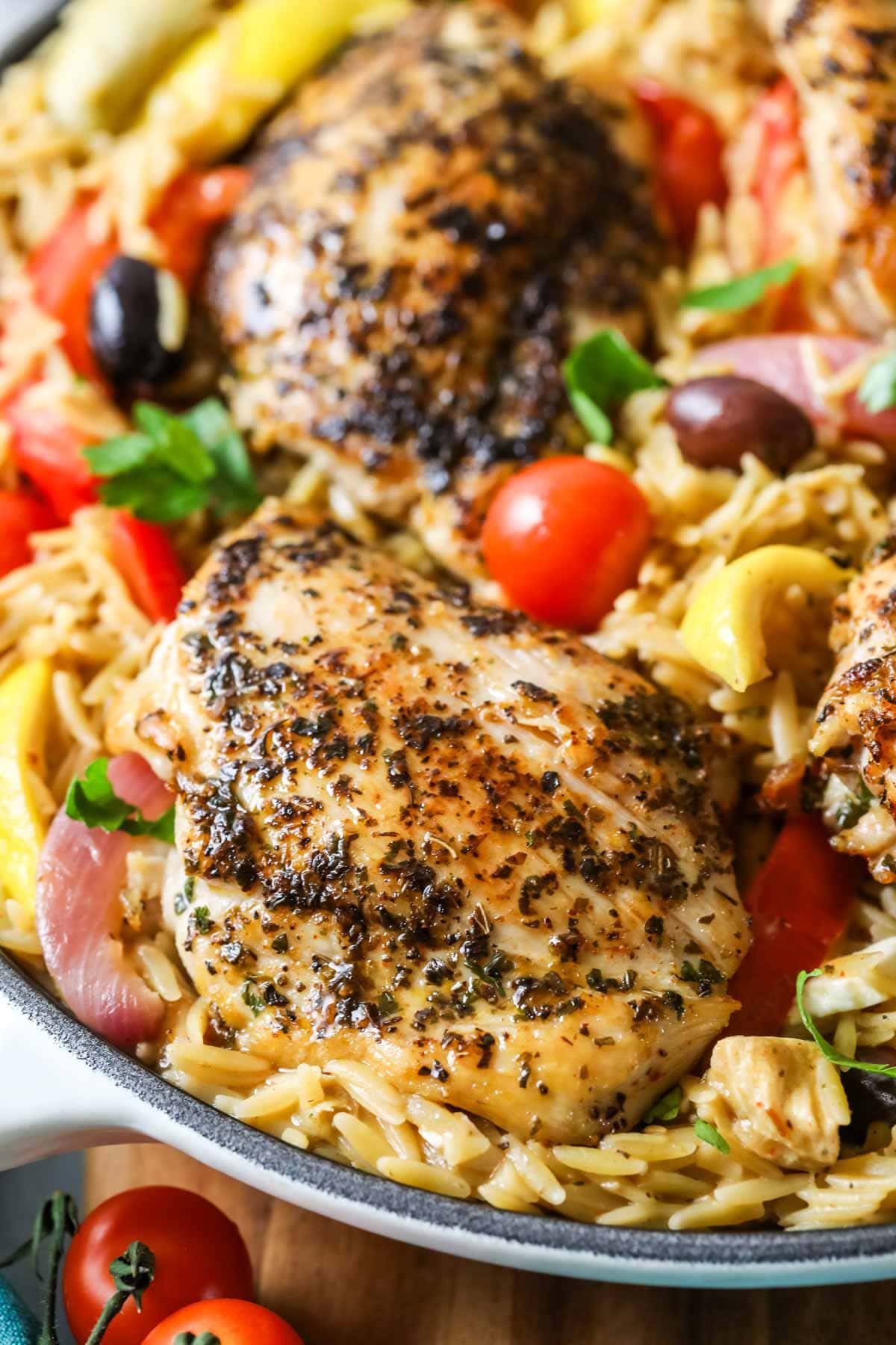 Close-up view of Greek chicken Orzo in a pan with tomatoes, olives, and artichokes.