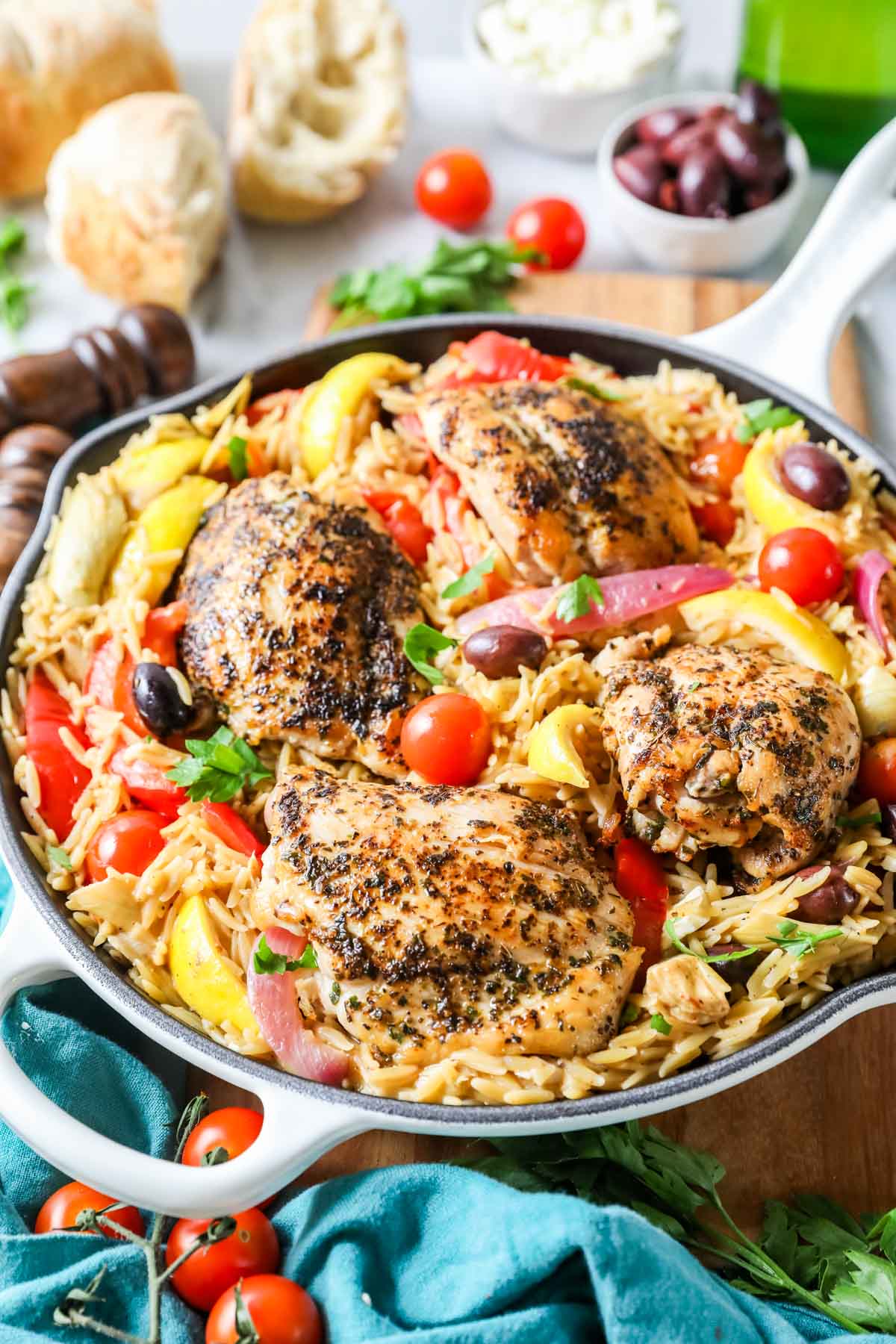 Greek chicken with Orzo, olives, artichokes, and tomatoes in a skillet.