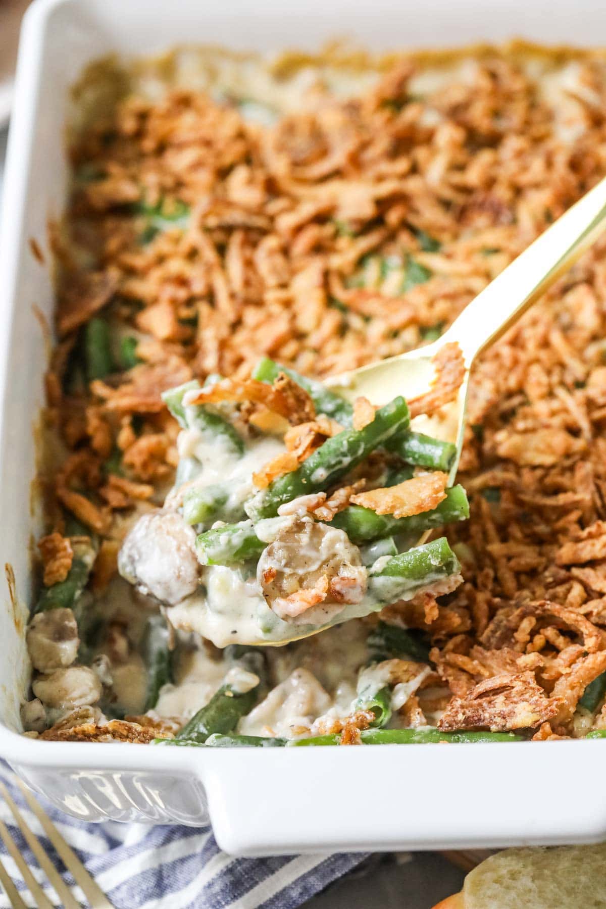 Green bean casserole being scooped out of a casserole dish with a gold spoon.