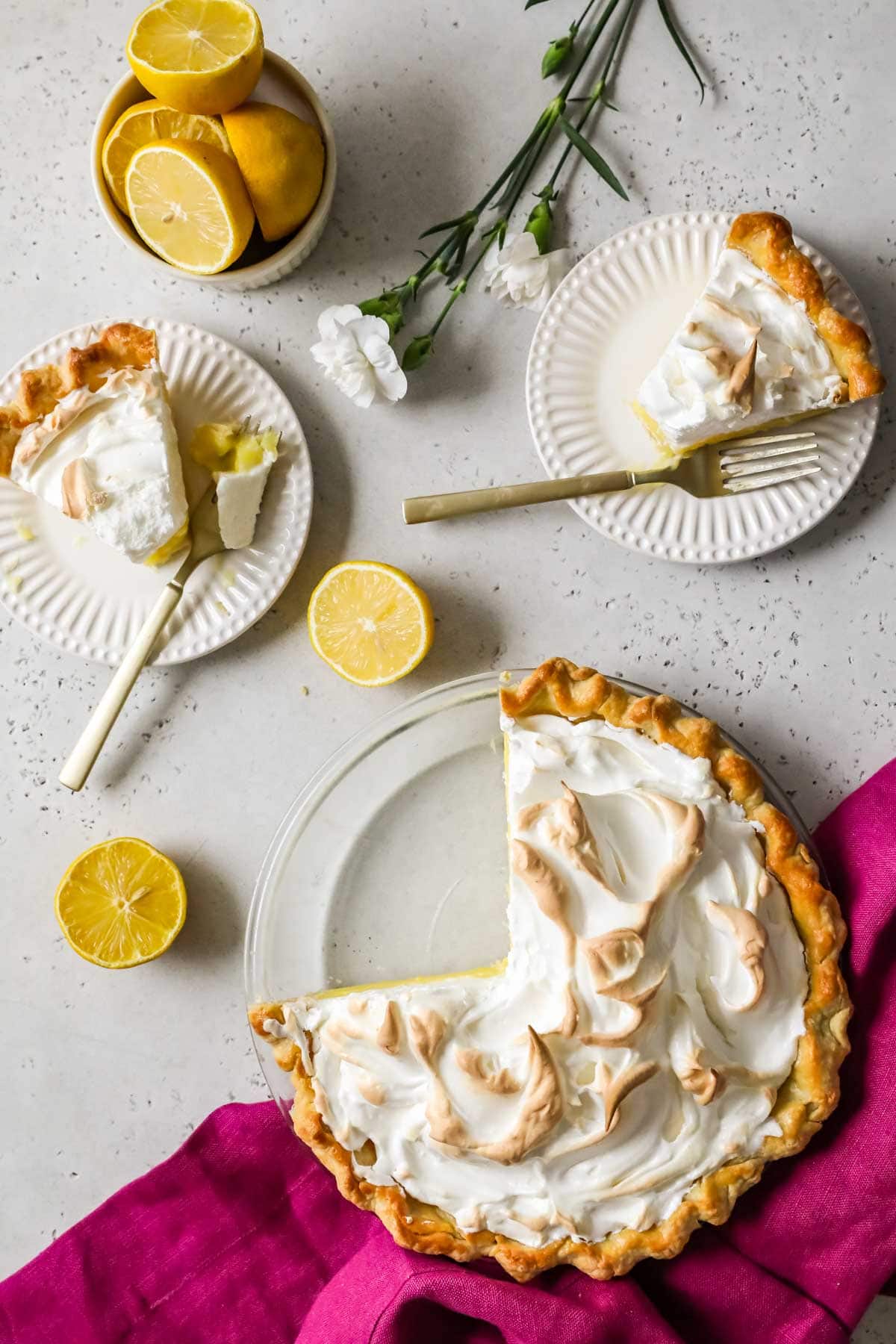 Overhead view of a lemon meringue pie with two slices removed and placed on plates.