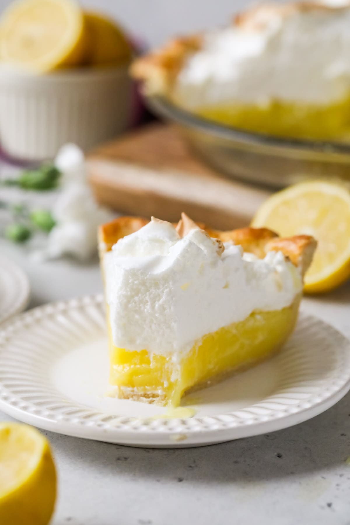 Slice of lemon meringue pie on a white plate with one bite missing.