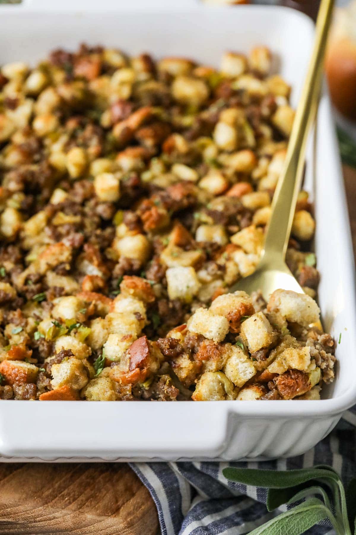 Gold spoon scooping sausage stuffing out of a casserole dish.