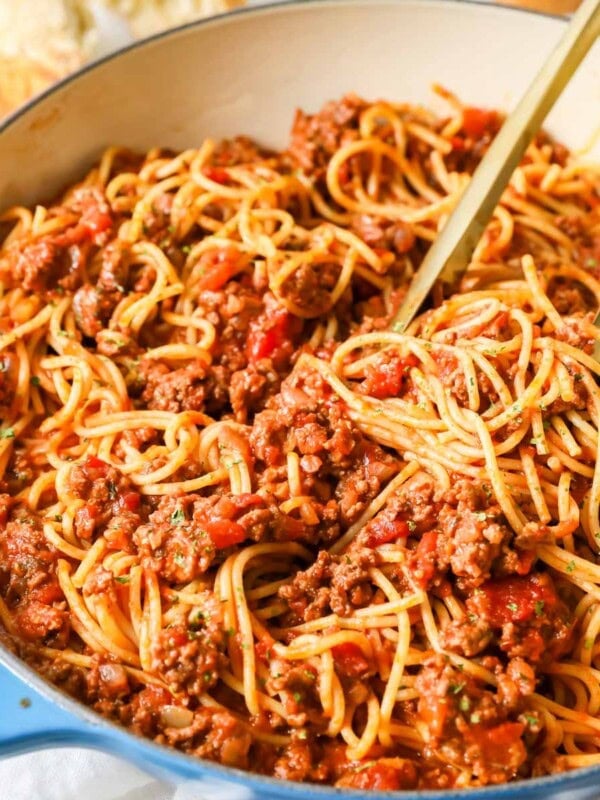 Tongs tossing spaghetti with meat sauce in a large pot.