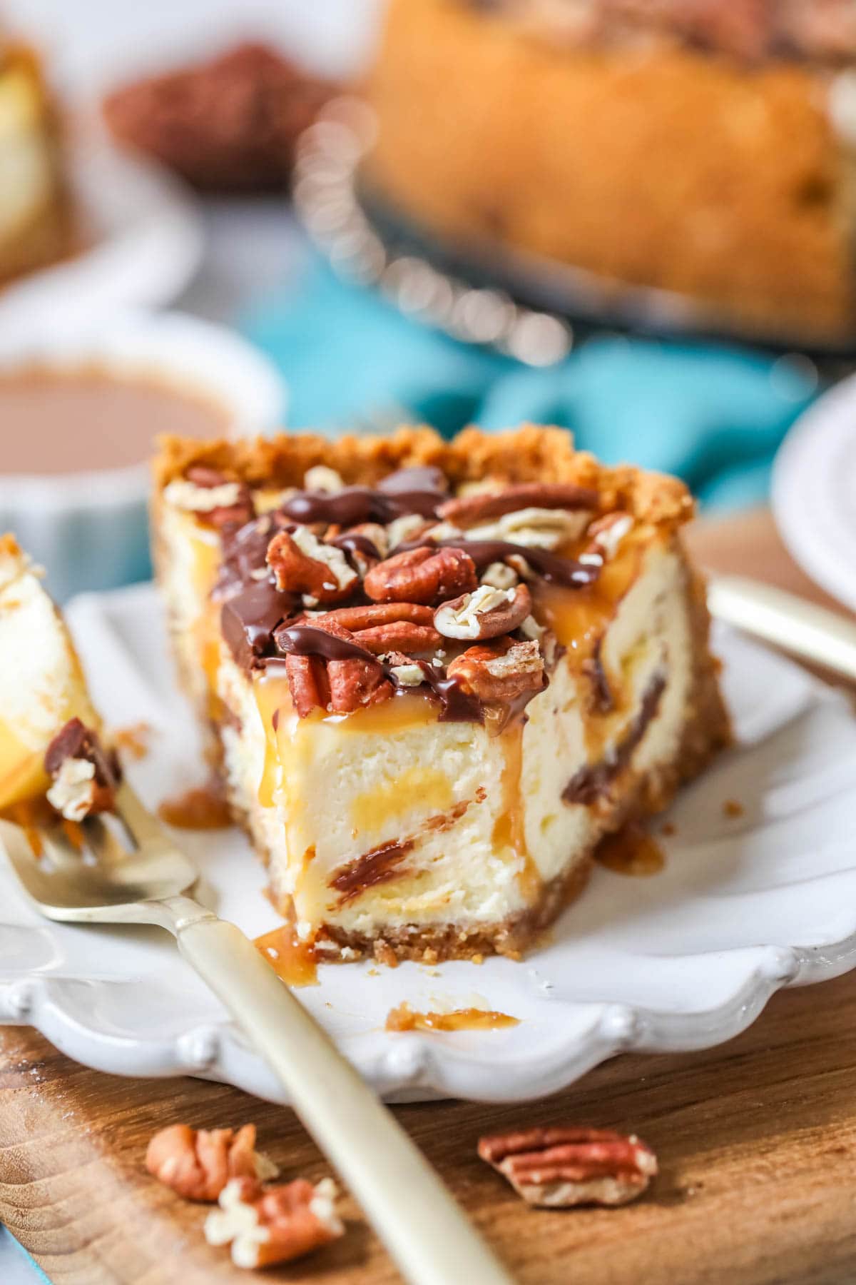 Close-up view of a slice of turtle cheesecake on a plate with one bite missing.