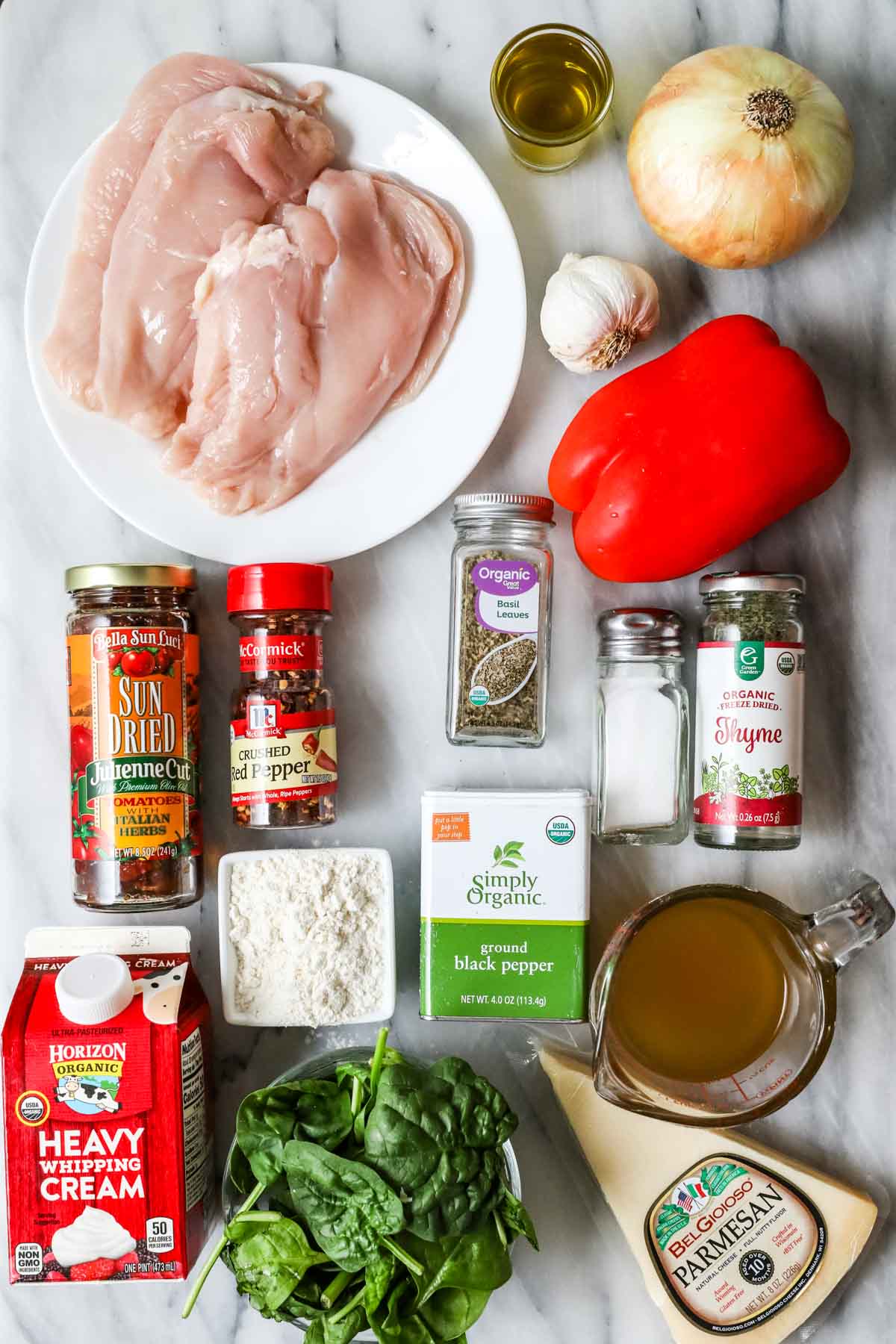 Overhead view of ingredients including chicken breasts, sun dried tomatoes, cream, spinach, and more.