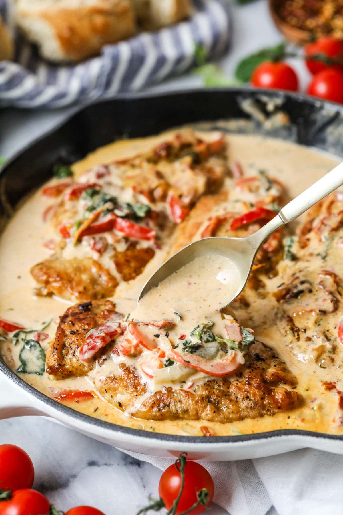 Cream sauce made with red peppers, spinach, and sun dried tomatoes being spooned over seared chicken.
